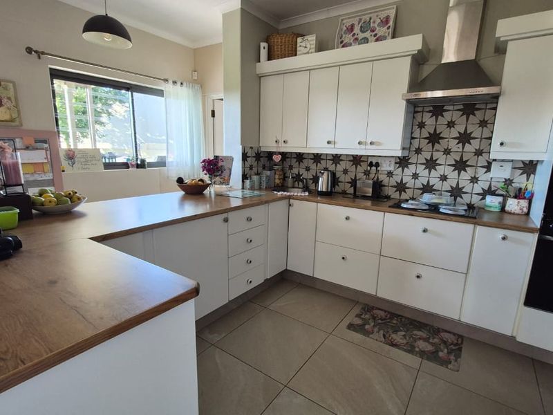 A functional kitchen featuring white cabinetry, wood-look laminate countertops, a patterned tiled backsplash, and integrated appliances including an oven and extractor fan.