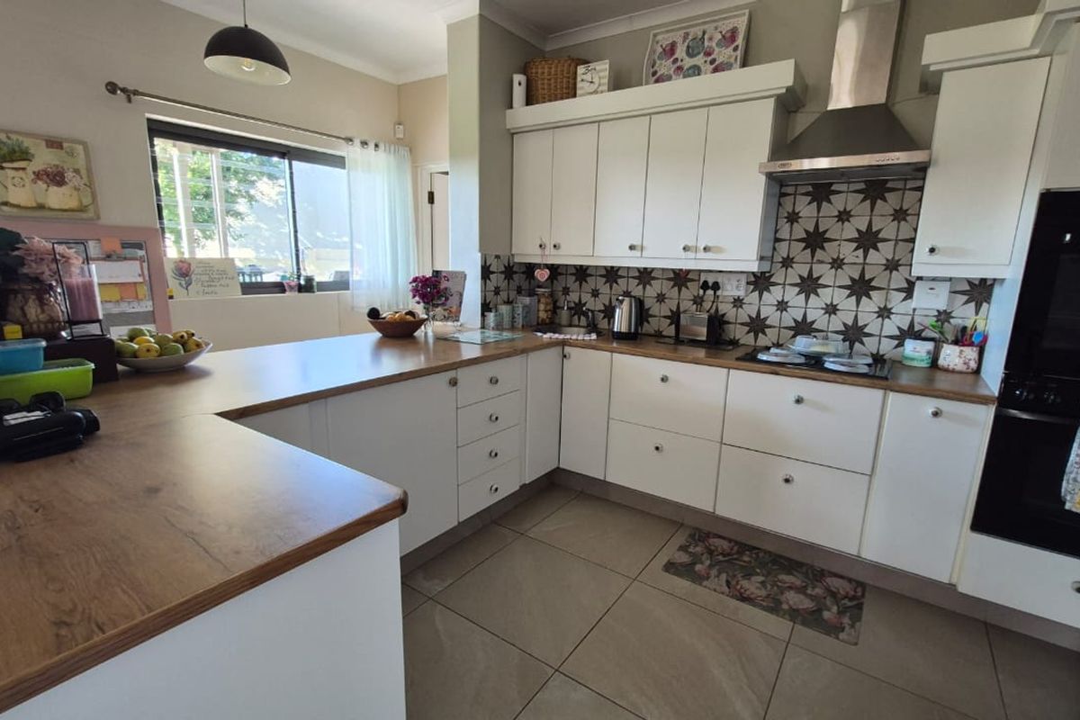 A functional kitchen featuring white cabinetry, wood-look laminate countertops, a patterned tiled backsplash, and integrated appliances including an oven and extractor fan.