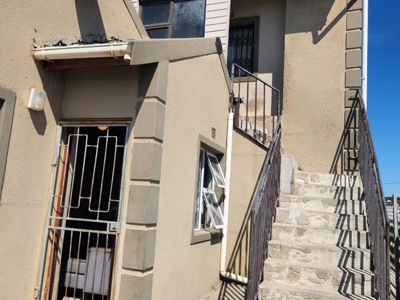 Exterior view of a multi-level residential property featuring an external staircase, security gates, and visible maintenance requirements on the facade and stairs.