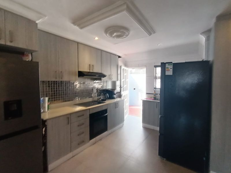 A functional kitchen featuring modern grey cabinetry, built-in oven and hob, tiled backsplash, and decorative ceiling detailing with direct access to an outdoor area.