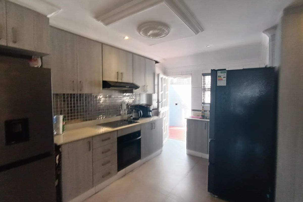 A functional kitchen featuring modern grey cabinetry, built-in oven and hob, tiled backsplash, and decorative ceiling detailing with direct access to an outdoor area.