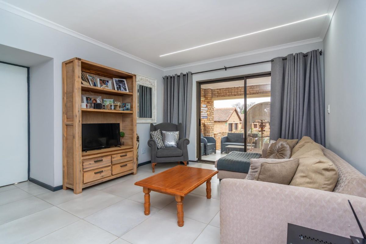 A bright living room featuring large format floor tiles, recessed ceiling lighting, and sliding glass doors providing direct access to a covered patio.