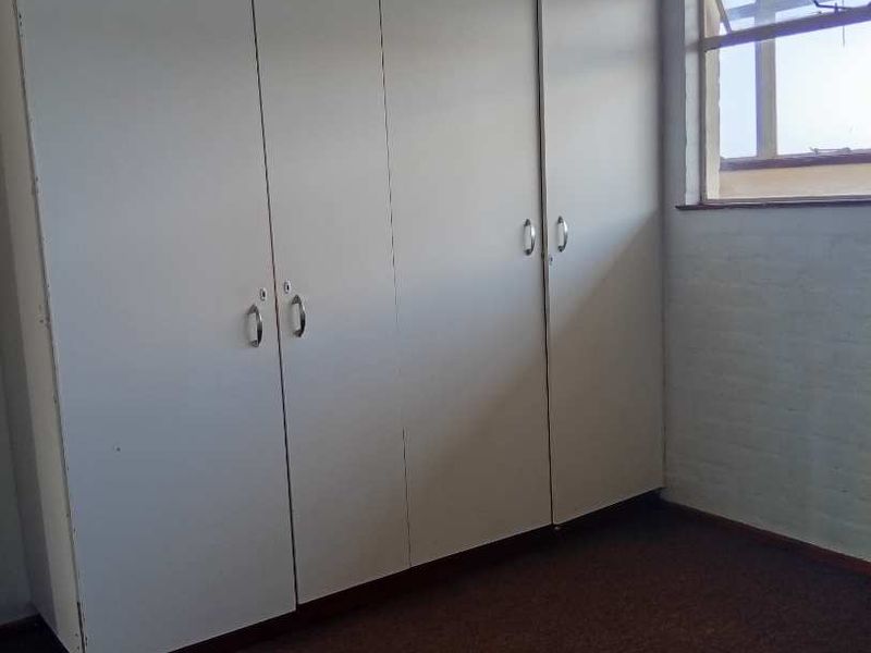A vacant bedroom featuring floor-to-ceiling built-in cupboards and a standard casement window, requiring cosmetic updates to the flooring and finishes.