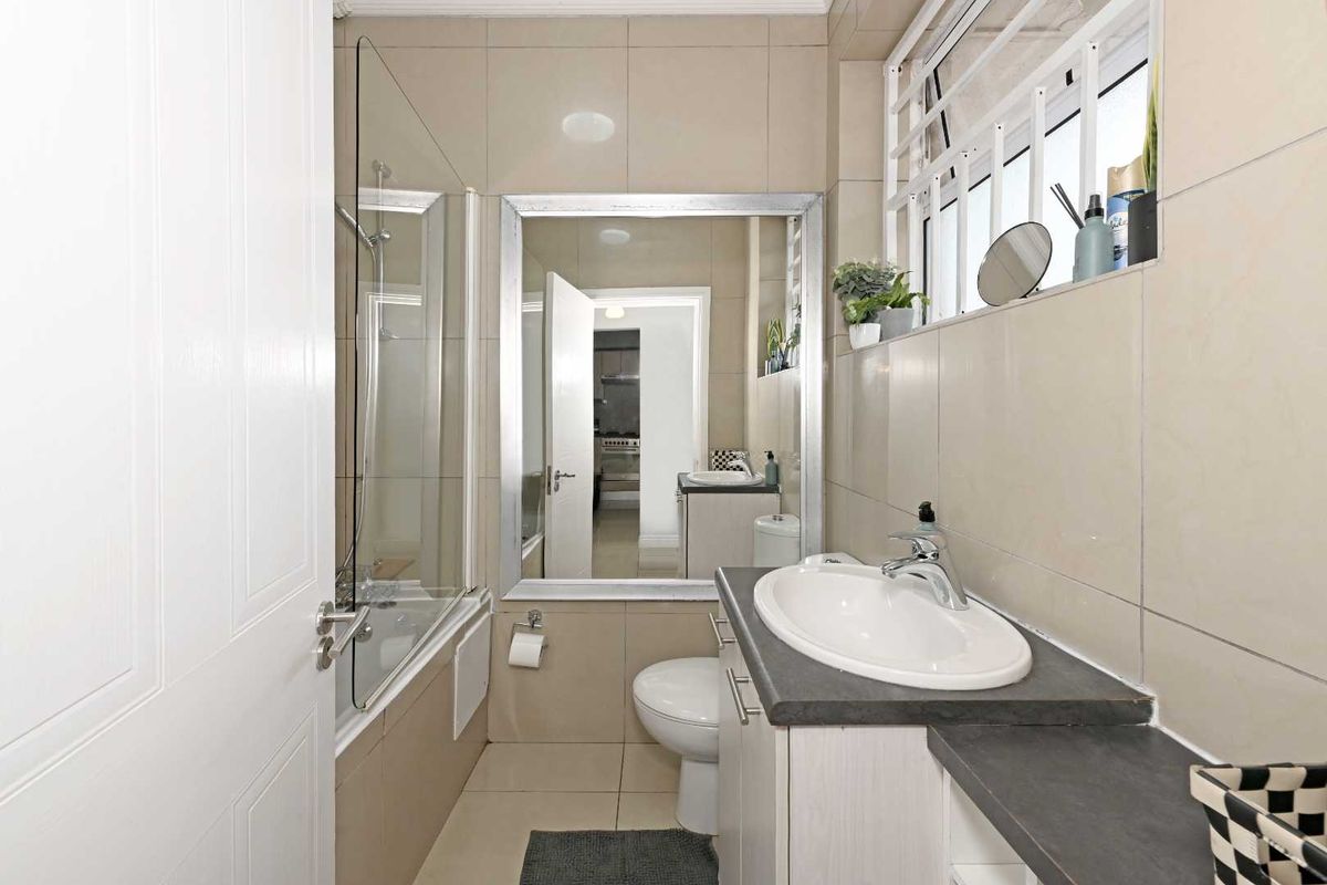 A functional bathroom featuring a vanity with a basin, a toilet, and a shower-over-bath combination with a glass screen and neutral wall tiling.
