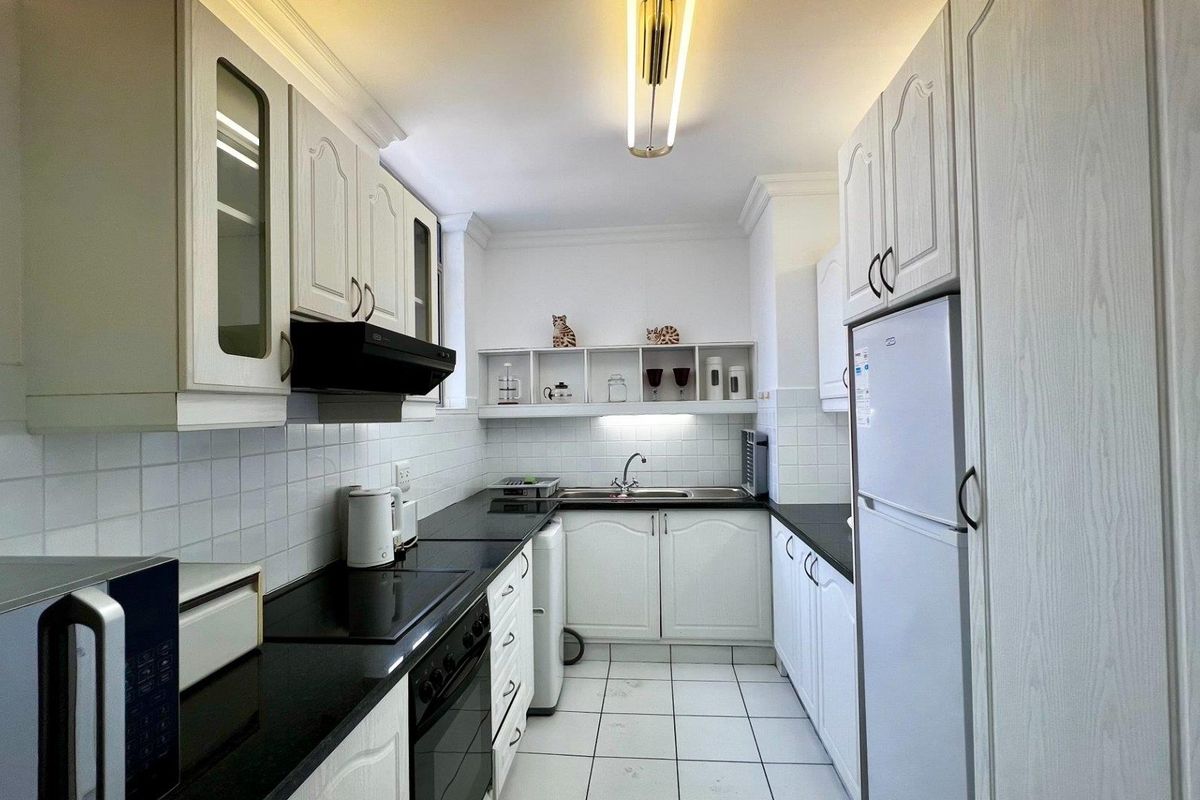 A functional galley-style kitchen featuring white cabinetry, black countertops, tiled backsplash, and integrated appliances, offering a clean and practical workspace.