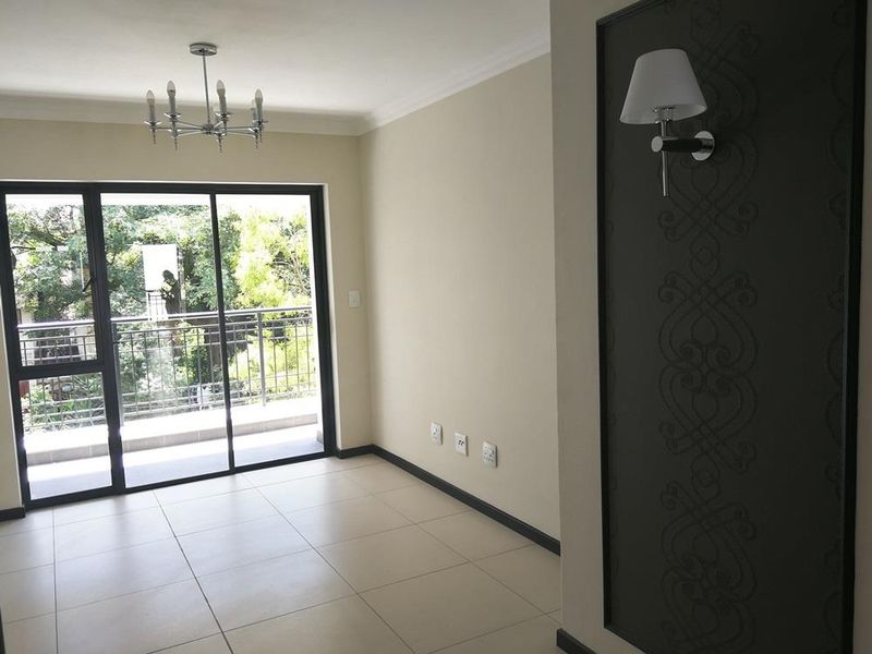 A bright, empty living area featuring neutral tiled floors, a decorative wall panel with sconce lighting, and sliding glass doors leading to a balcony.