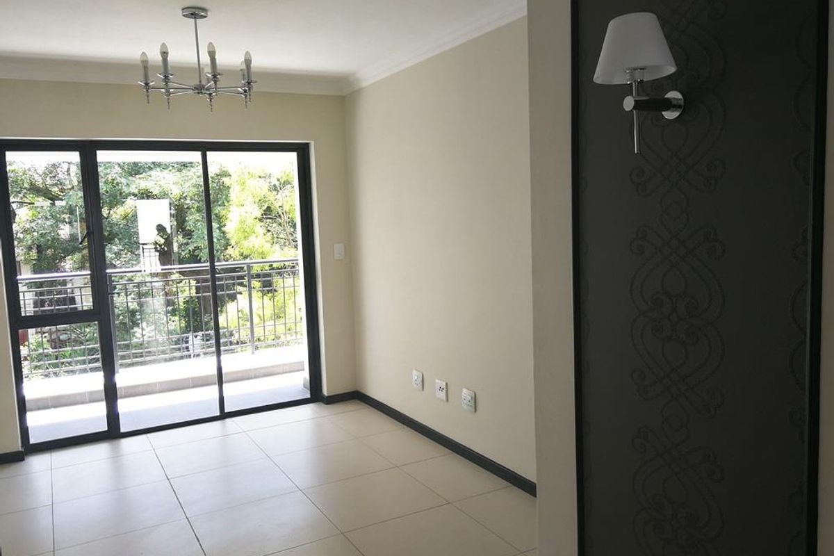 A bright, empty living area featuring neutral tiled floors, a decorative wall panel with sconce lighting, and sliding glass doors leading to a balcony.