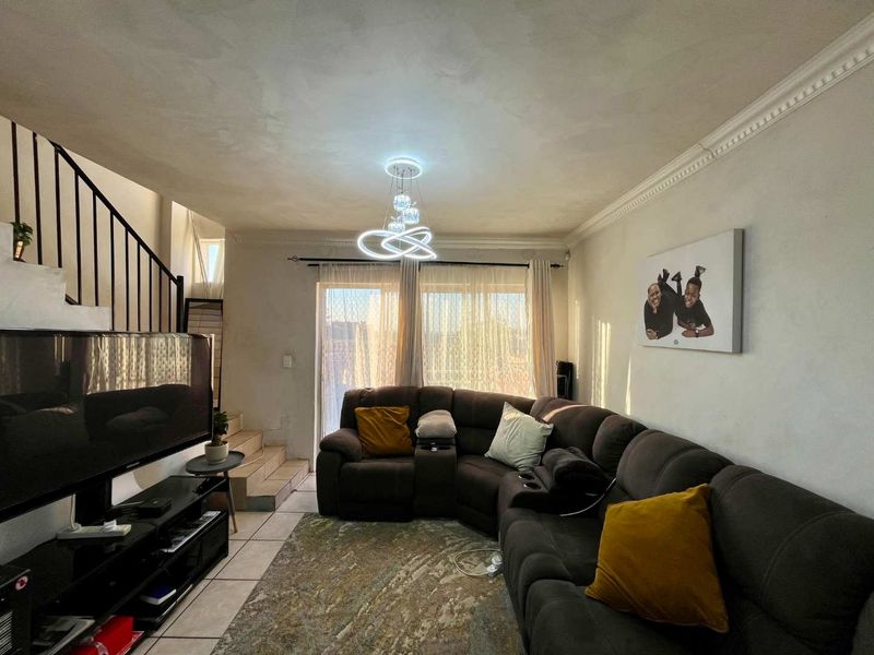 A living room featuring tiled flooring, crown molding, and a staircase with a metal balustrade, leading to a sliding glass door with natural light.