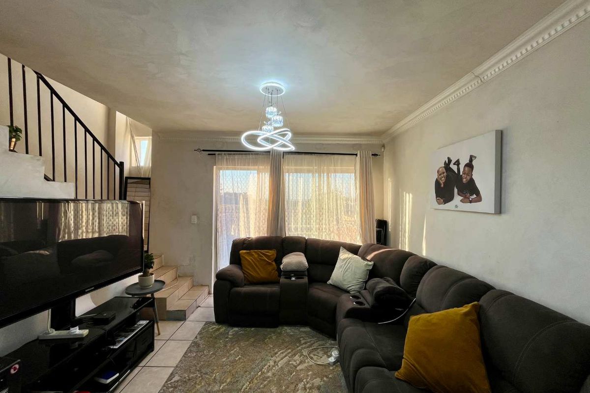 A living room featuring tiled flooring, crown molding, and a staircase with a metal balustrade, leading to a sliding glass door with natural light.