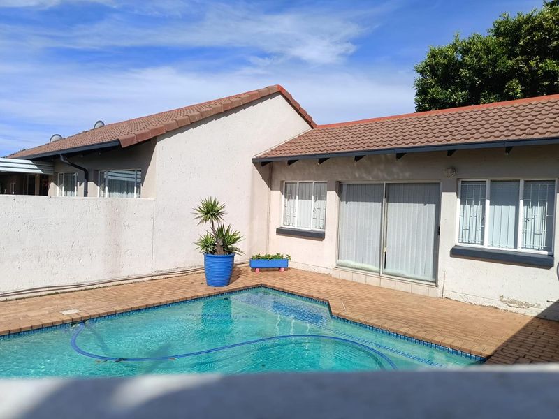 Rear exterior view of the townhouse featuring a swimming pool, brick paved patio area, and sliding glass door access to the main living space.