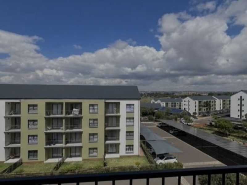 Elevated view from a balcony overlooking the apartment complex, featuring covered parking bays and surrounding residential buildings.