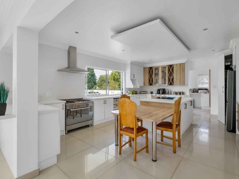 Modern kitchen featuring white cabinetry, a central island, stainless steel appliances, and tiled flooring, with an adjacent scullery area visible.