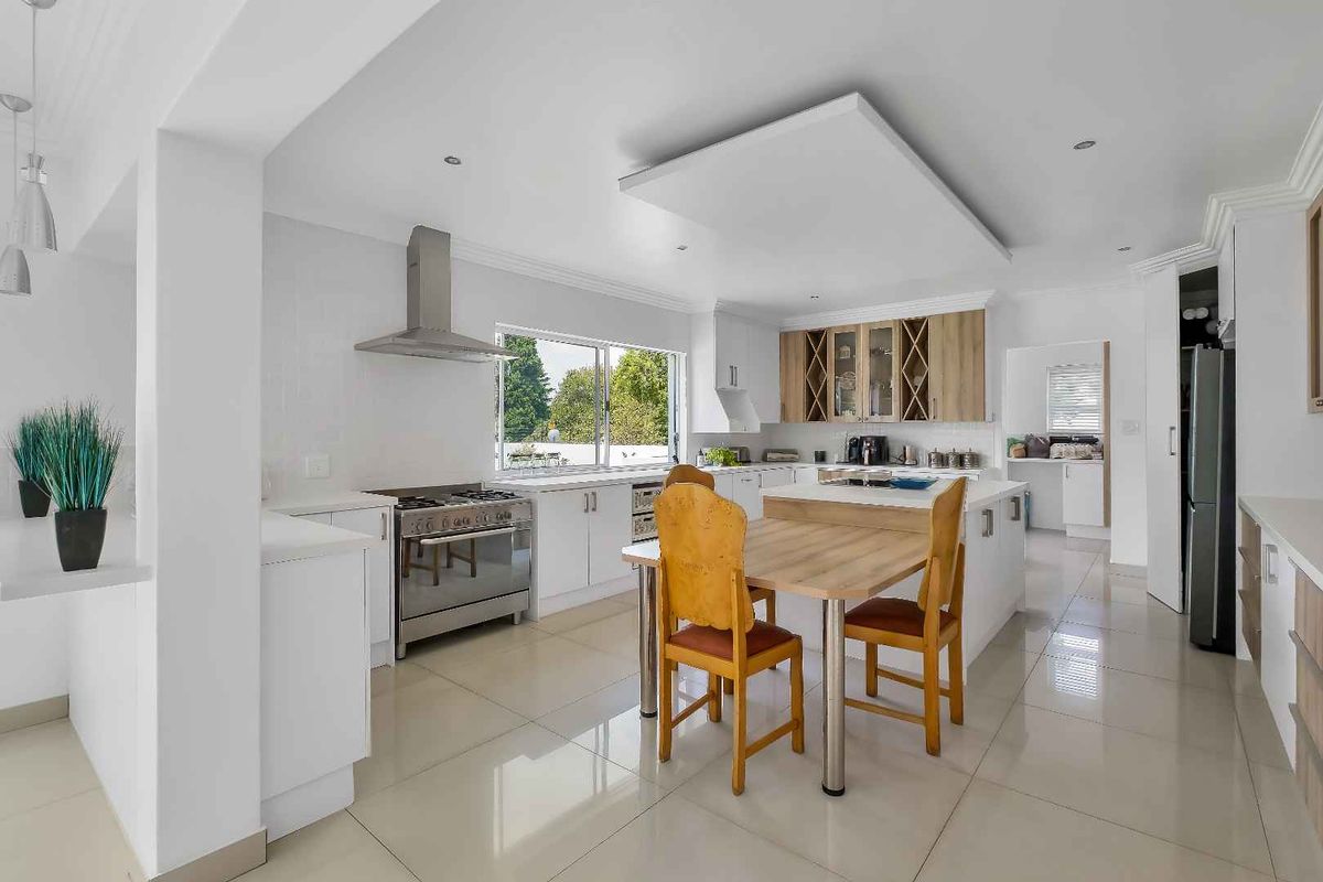 Modern kitchen featuring white cabinetry, a central island, stainless steel appliances, and tiled flooring, with an adjacent scullery area visible.