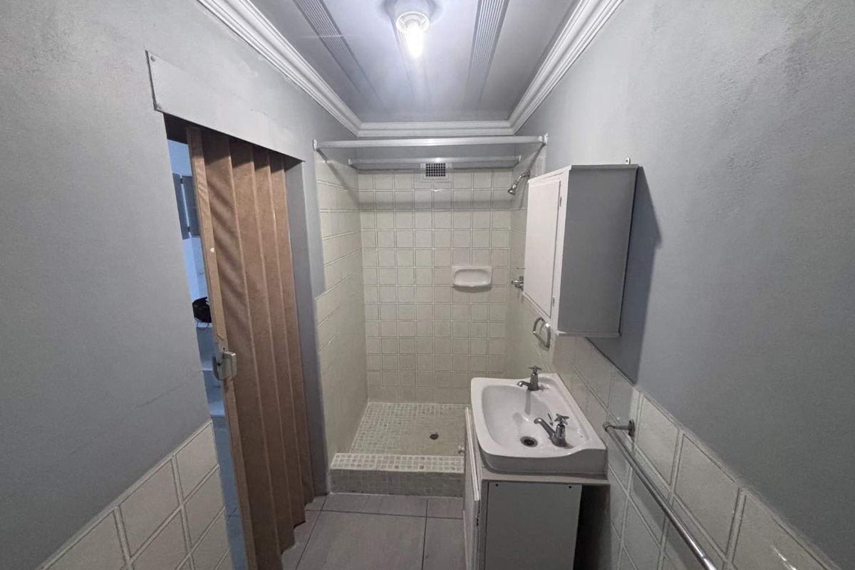 A compact bathroom featuring a tiled shower enclosure, a wall-mounted vanity basin, and a folding door entrance.