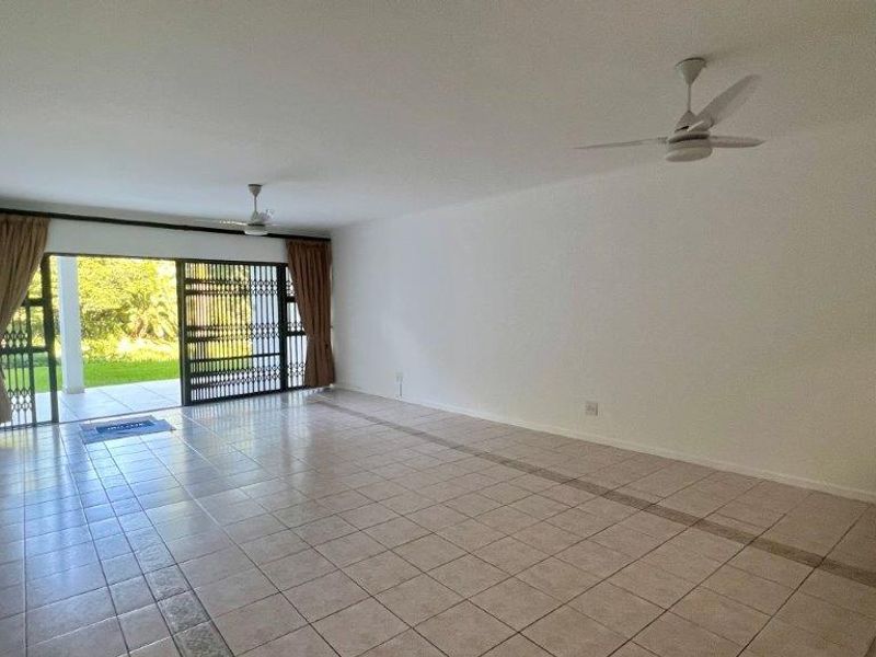 Spacious, empty living area featuring tiled flooring, ceiling fans, and a large sliding glass door providing access to the outdoor patio.