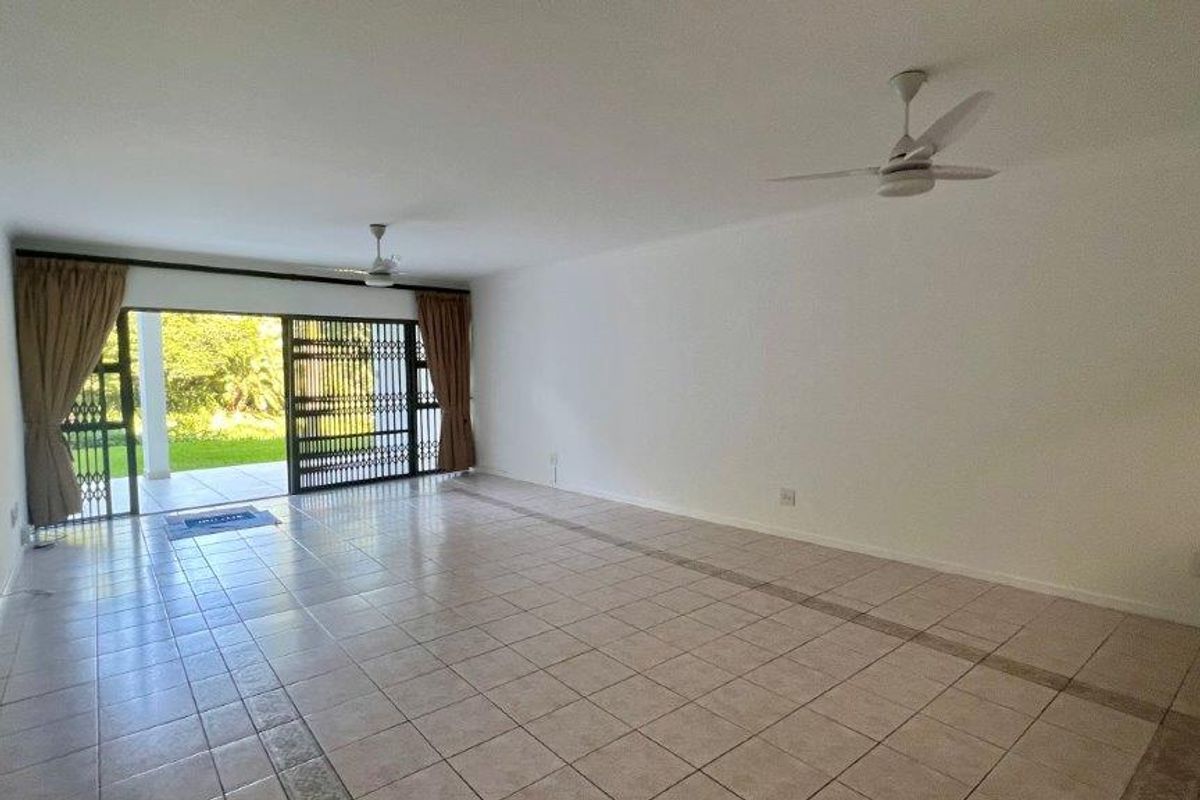 Spacious, empty living area featuring tiled flooring, ceiling fans, and a large sliding glass door providing access to the outdoor patio.