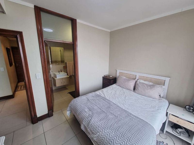 A bedroom featuring tiled flooring, wooden door frames, and an adjoining en-suite bathroom with a modern vanity.