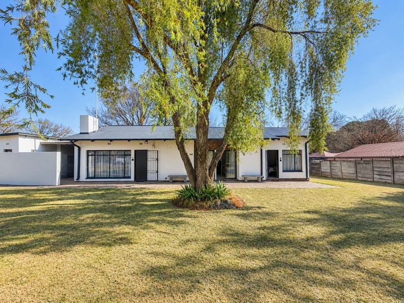 Rear view of the house featuring a paved patio area, established garden, and secure access points under a corrugated metal roof.