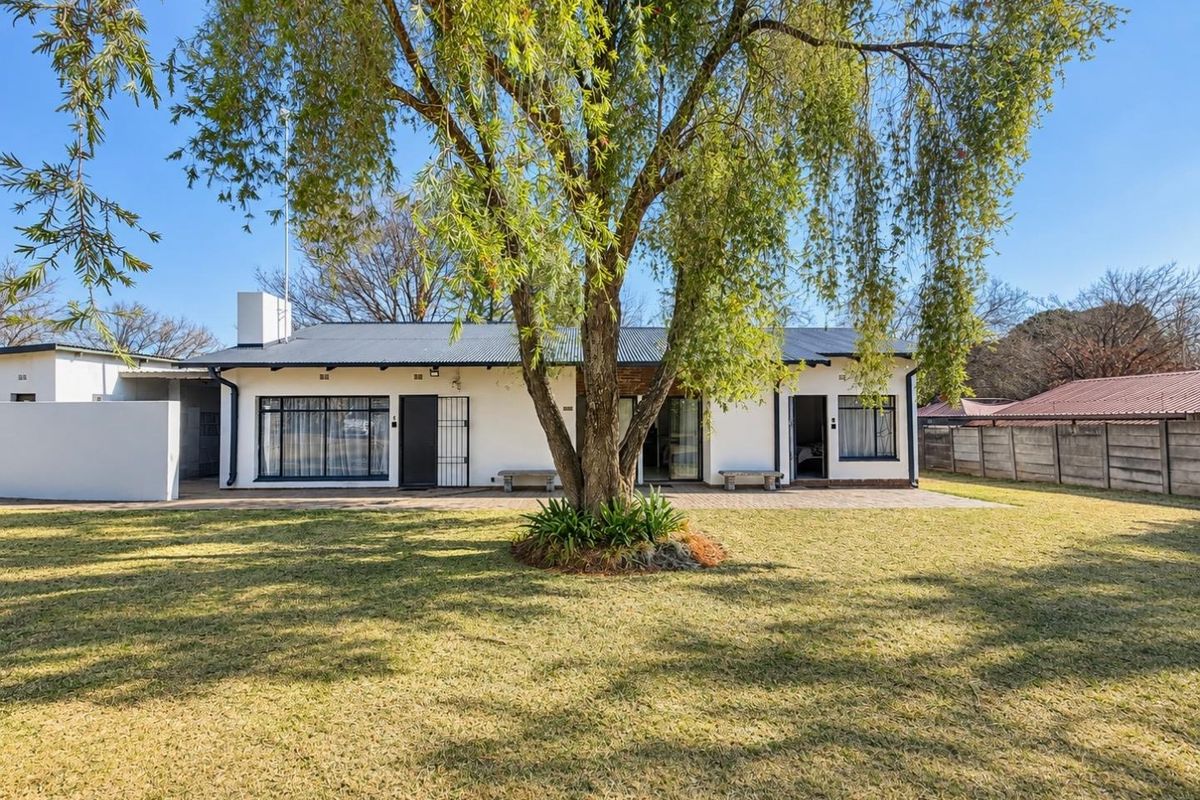 Rear view of the house featuring a paved patio area, established garden, and secure access points under a corrugated metal roof.