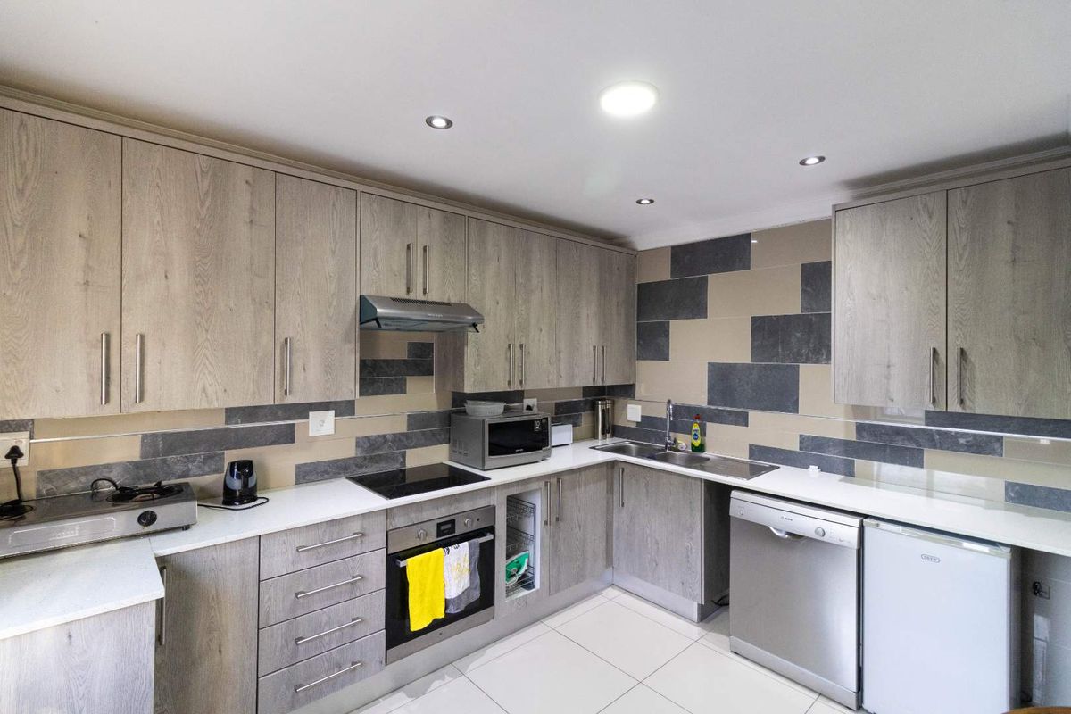 Modern kitchen featuring wood-grain cabinetry, stone countertops, integrated appliances, and a contemporary tiled backsplash with recessed lighting.