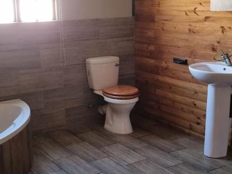A bathroom featuring a pedestal basin, toilet, and corner bathtub, finished with wood paneling and tiled flooring.