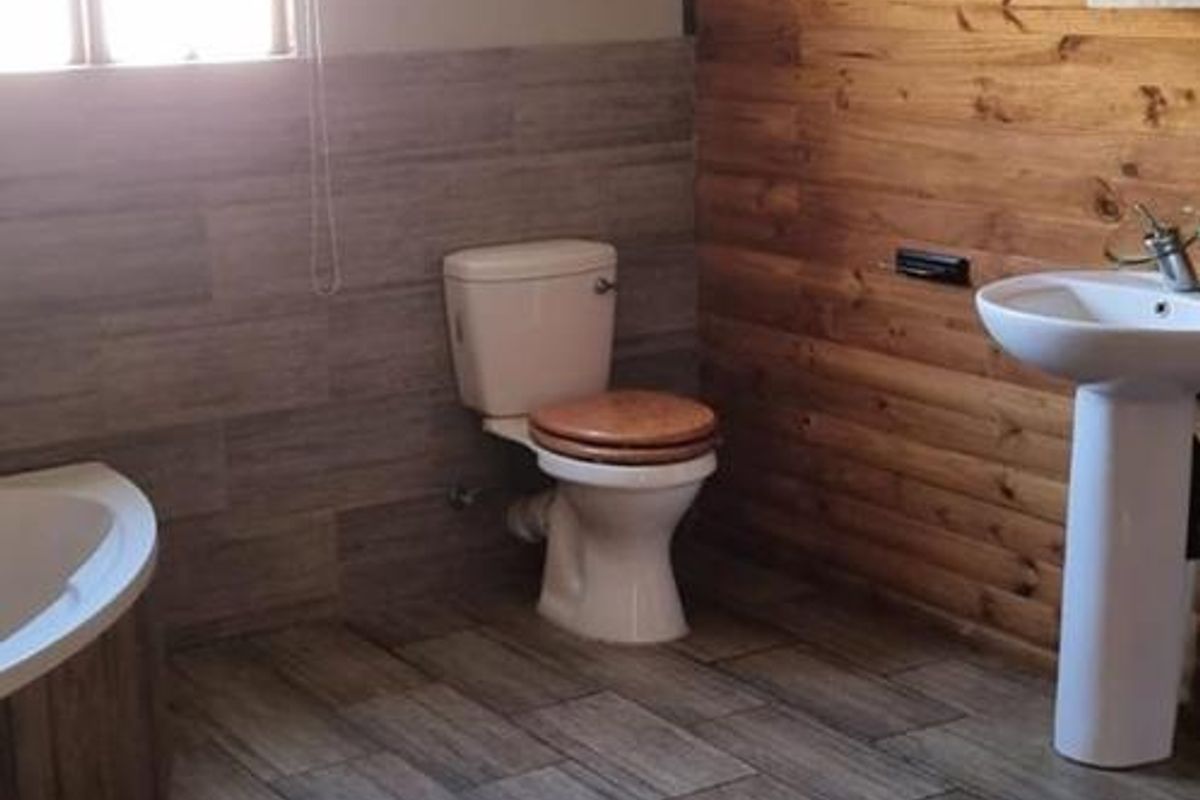 A bathroom featuring a pedestal basin, toilet, and corner bathtub, finished with wood paneling and tiled flooring.