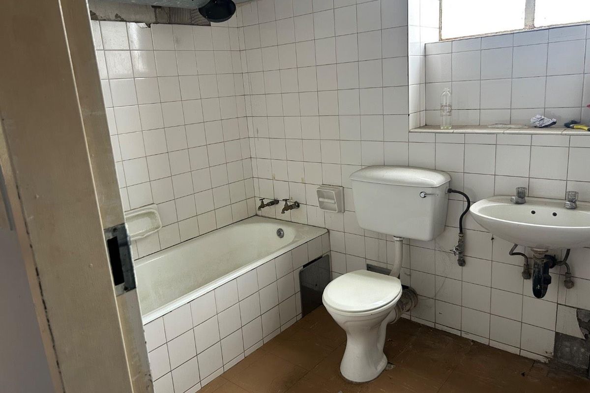 A dated bathroom featuring a standard bathtub, pedestal sink, and toilet, requiring significant renovation and modernization of finishes and fixtures.