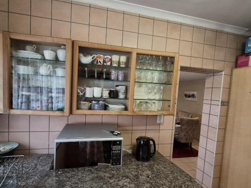 A kitchen area featuring built-in glass-fronted cabinetry, granite countertops, and tiled wall finishes, with a doorway leading to an adjacent living space.