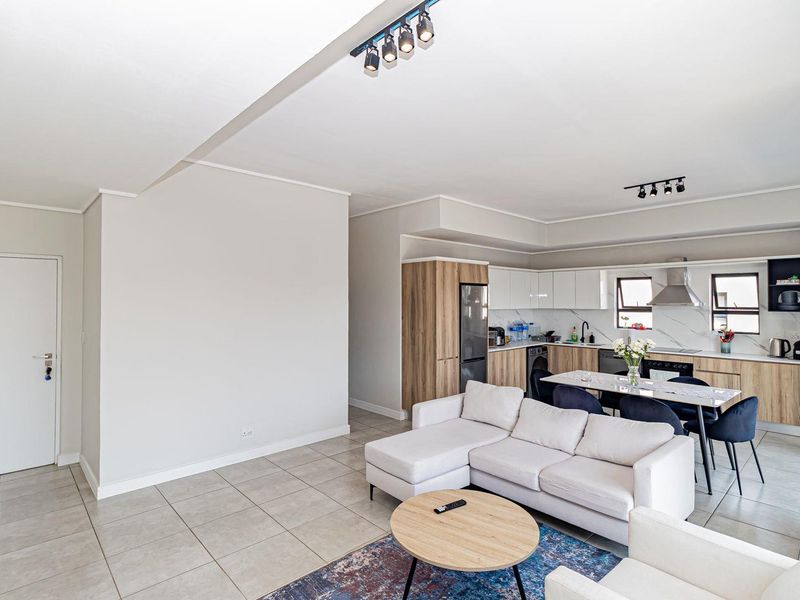 Modern open-plan living area featuring a contemporary kitchen with sleek cabinetry, integrated appliances, and neutral tiled flooring throughout the space.