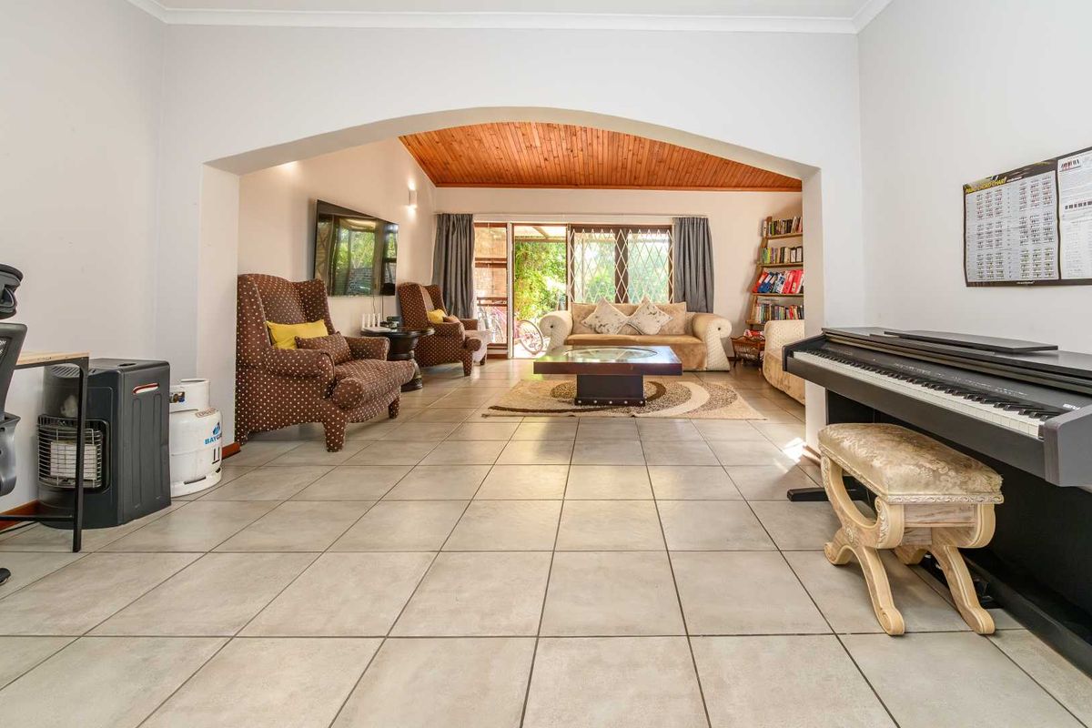 Spacious living area featuring large floor tiles, a distinctive timber-clad vaulted ceiling, and an open archway leading to a bright rear patio space.