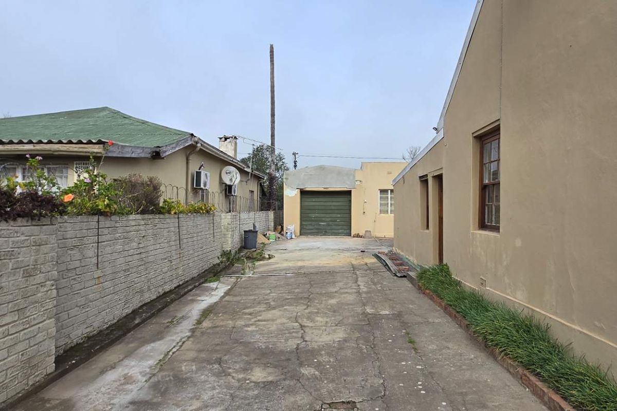 A view of the rear exterior area featuring a concrete driveway, brick boundary wall, and a detached garage structure.