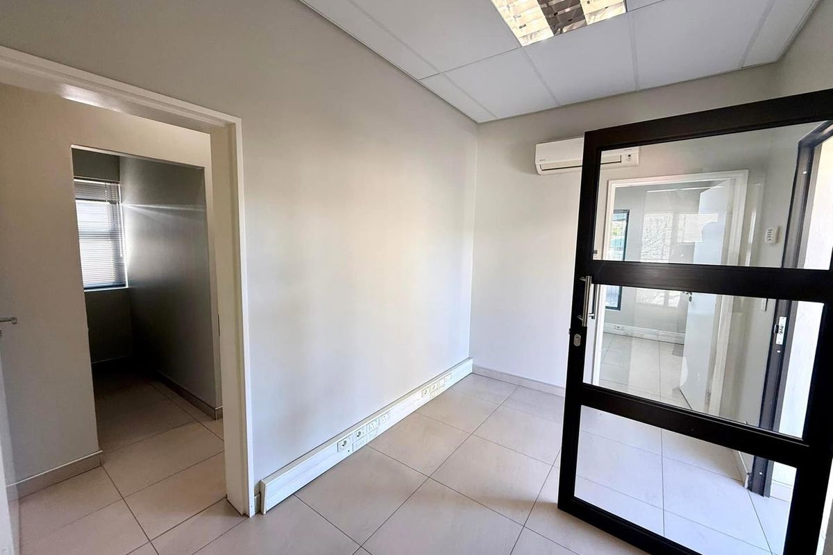 A clean, empty office space featuring tiled flooring, a suspended ceiling with recessed lighting, a wall-mounted air conditioner, and integrated electrical trunking.