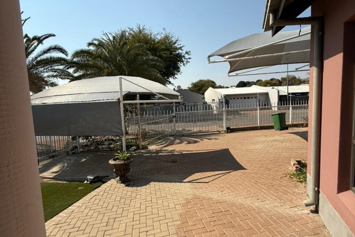 A paved rear patio area featuring shade sails and metal perimeter fencing, providing an outdoor space for relaxation.