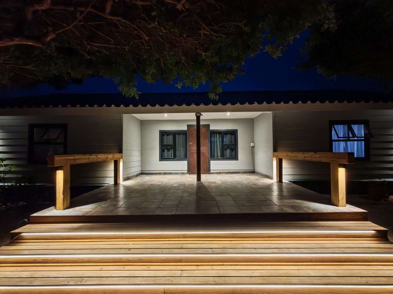 A beautifully illuminated covered patio featuring timber decking, integrated step lighting, and modern tiled flooring, creating an inviting outdoor entrance area.