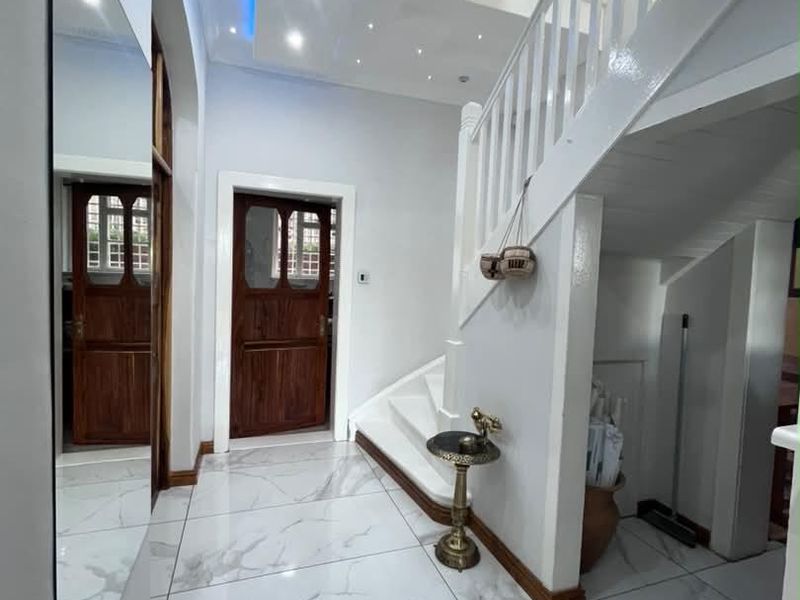 Bright and modern entrance hall featuring polished marble-look floor tiles, a classic staircase, and sophisticated recessed ceiling lighting with blue accent cove lighting.