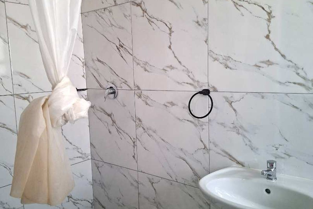 A bathroom featuring marble-effect wall tiling, a pedestal basin, and a walk-in shower area with a checkered tile floor.