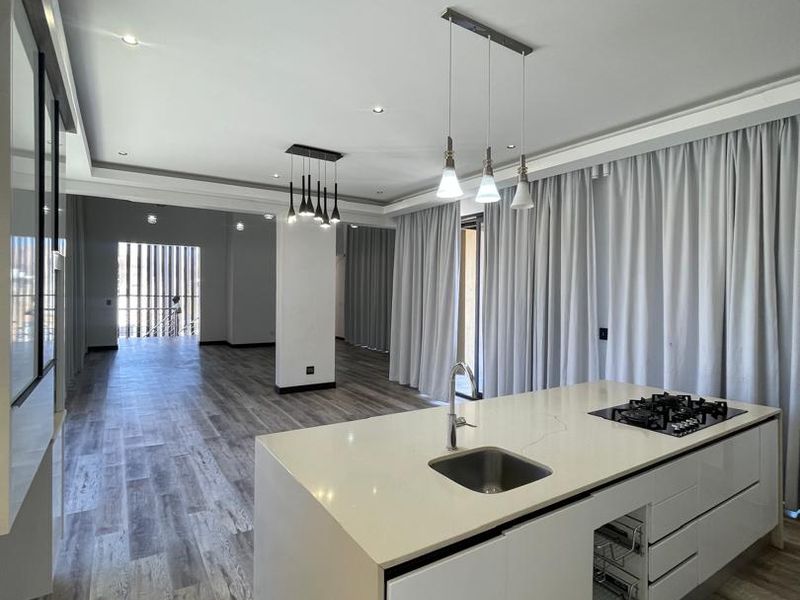 Spacious open-plan living area featuring a modern kitchen island with integrated gas cooktop, sleek cabinetry, and contemporary pendant lighting throughout the bright, airy space.