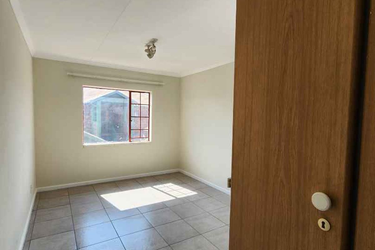 A bright, empty bedroom featuring neutral wall paint, tiled flooring, and a built-in cupboard, offering a clean canvas for personalization.
