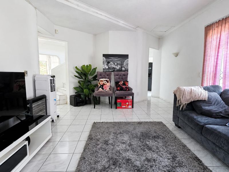 A bright living room featuring white tiled flooring and large windows with vertical blinds, offering a neutral base for interior design updates.