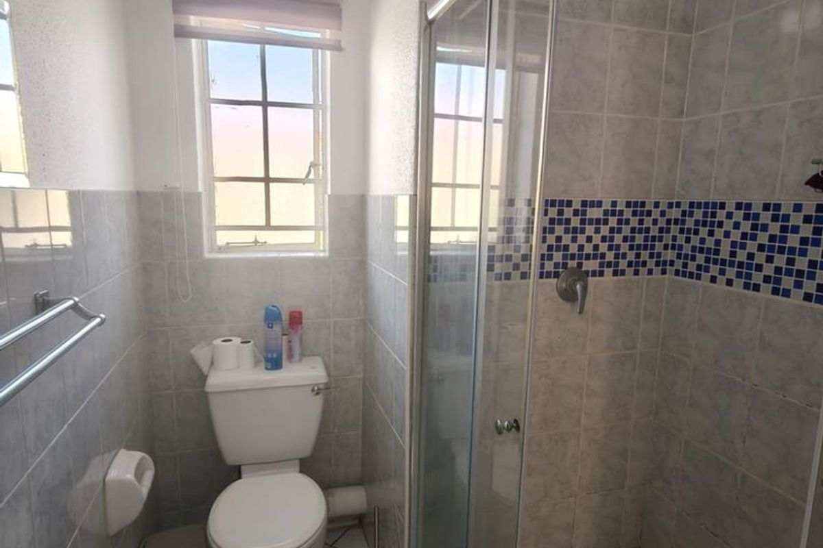 A functional bathroom featuring a glass-enclosed shower, toilet, and tiled finishes throughout, providing a practical layout for daily use.