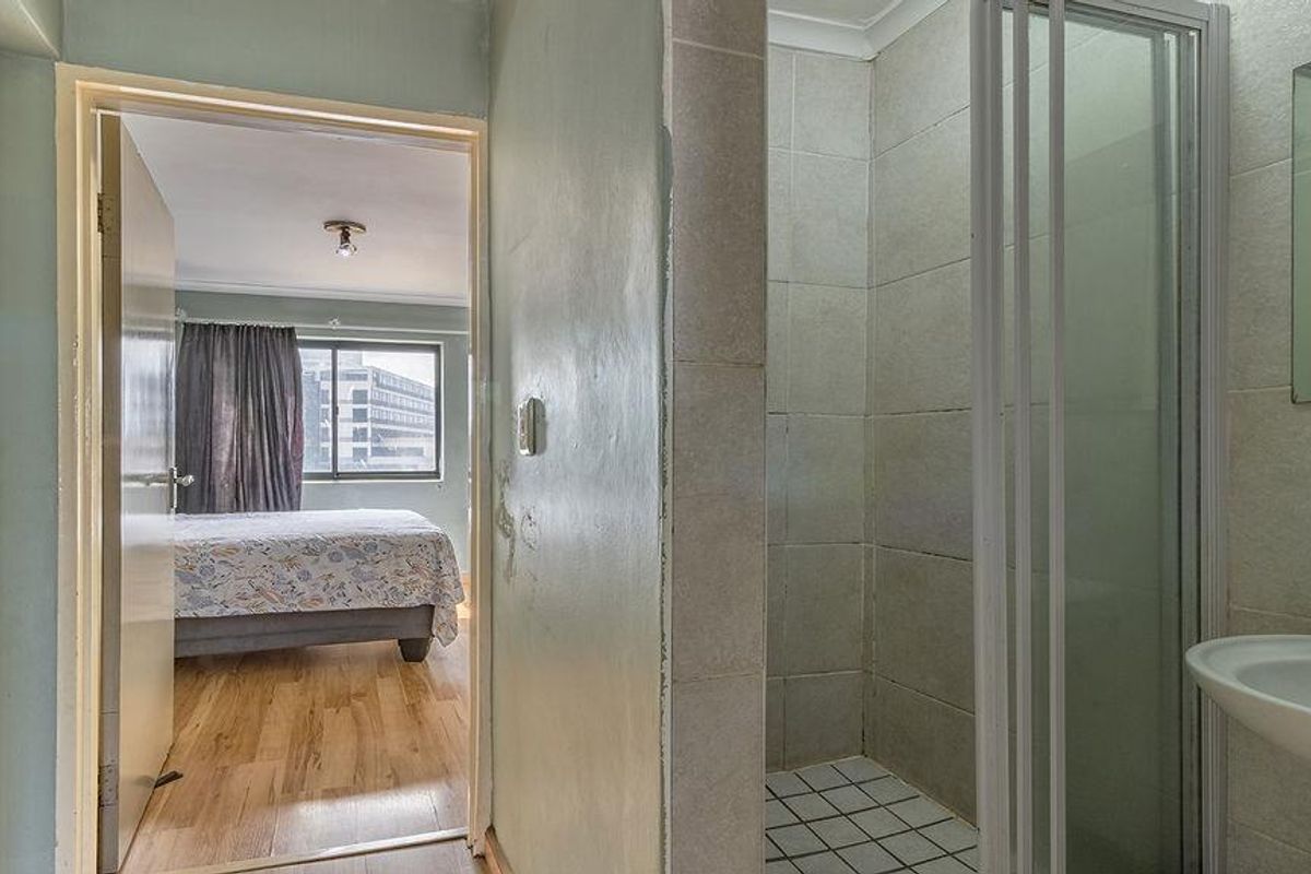 A bathroom featuring a shower enclosure and pedestal basin, with a view through the doorway into an adjacent bedroom with timber flooring.