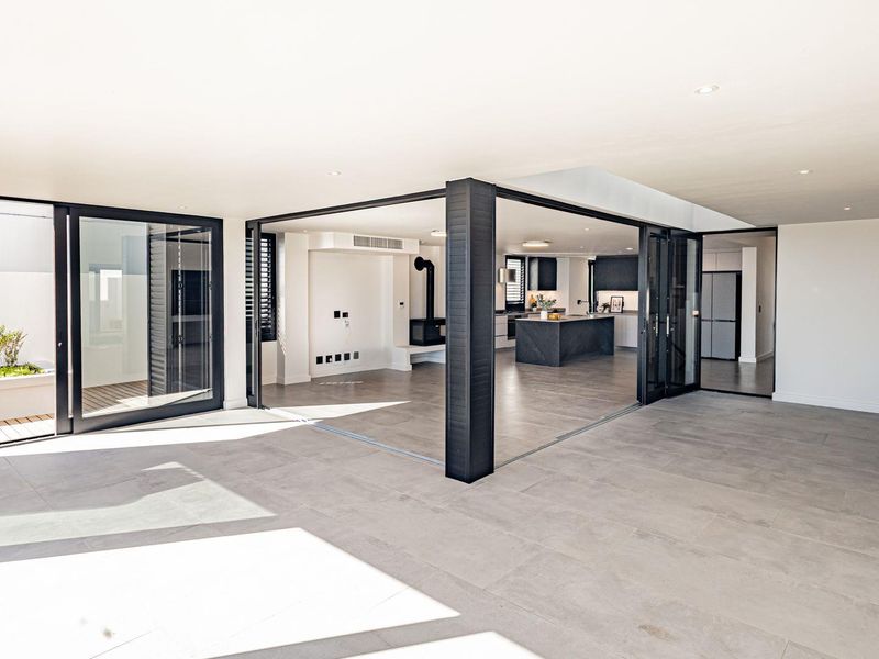 Spacious open-plan living area featuring large format floor tiles, seamless indoor-outdoor flow through sliding glass doors, and a modern kitchen with a central island.