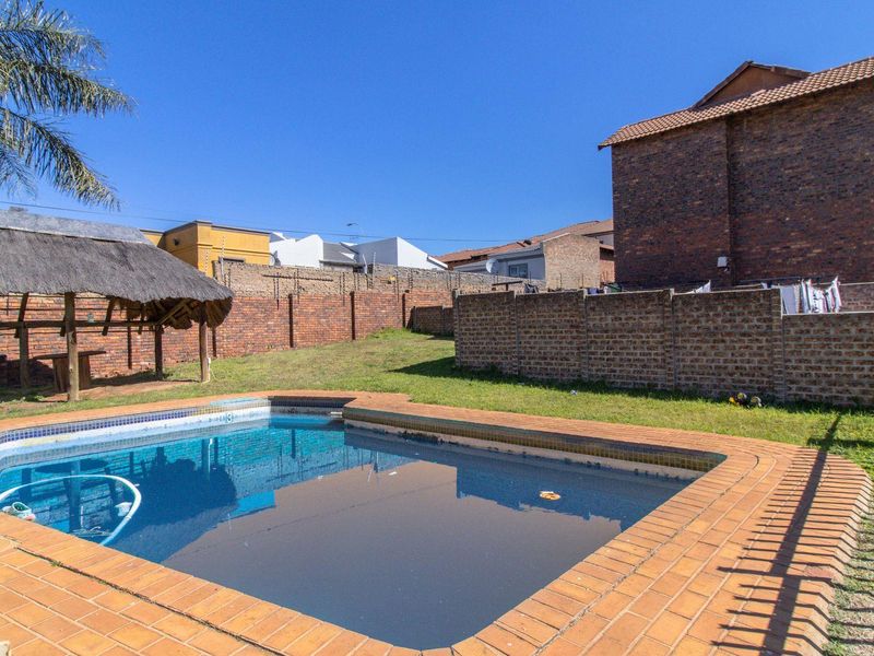 Outdoor area featuring a swimming pool, brick-paved surround, and a thatched lapa structure set within a private garden with perimeter brick walling.