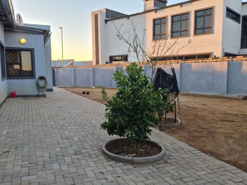 Rear exterior view featuring a paved patio area, perimeter wall with electric fencing, and an open garden space awaiting landscaping.