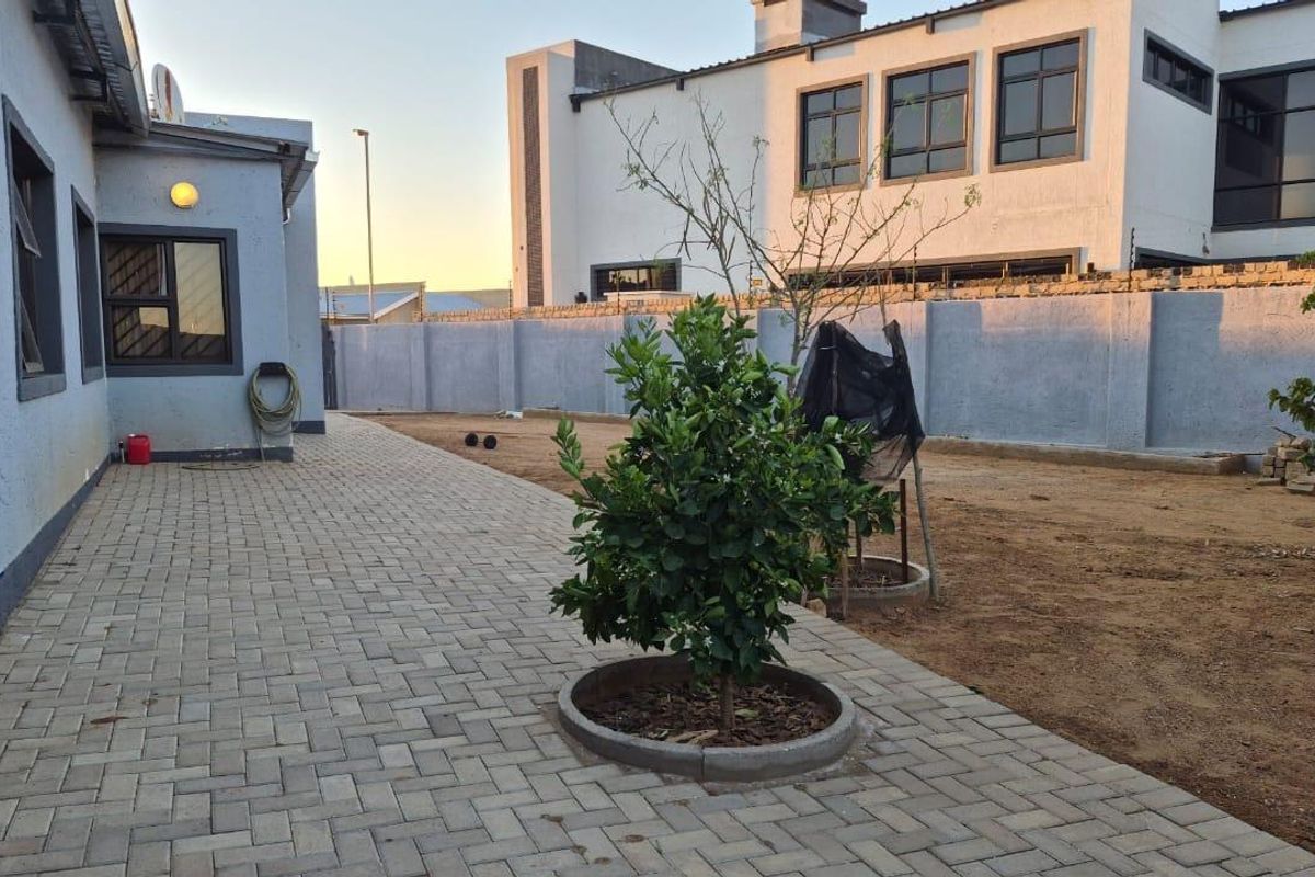 Rear exterior view featuring a paved patio area, perimeter wall with electric fencing, and an open garden space awaiting landscaping.