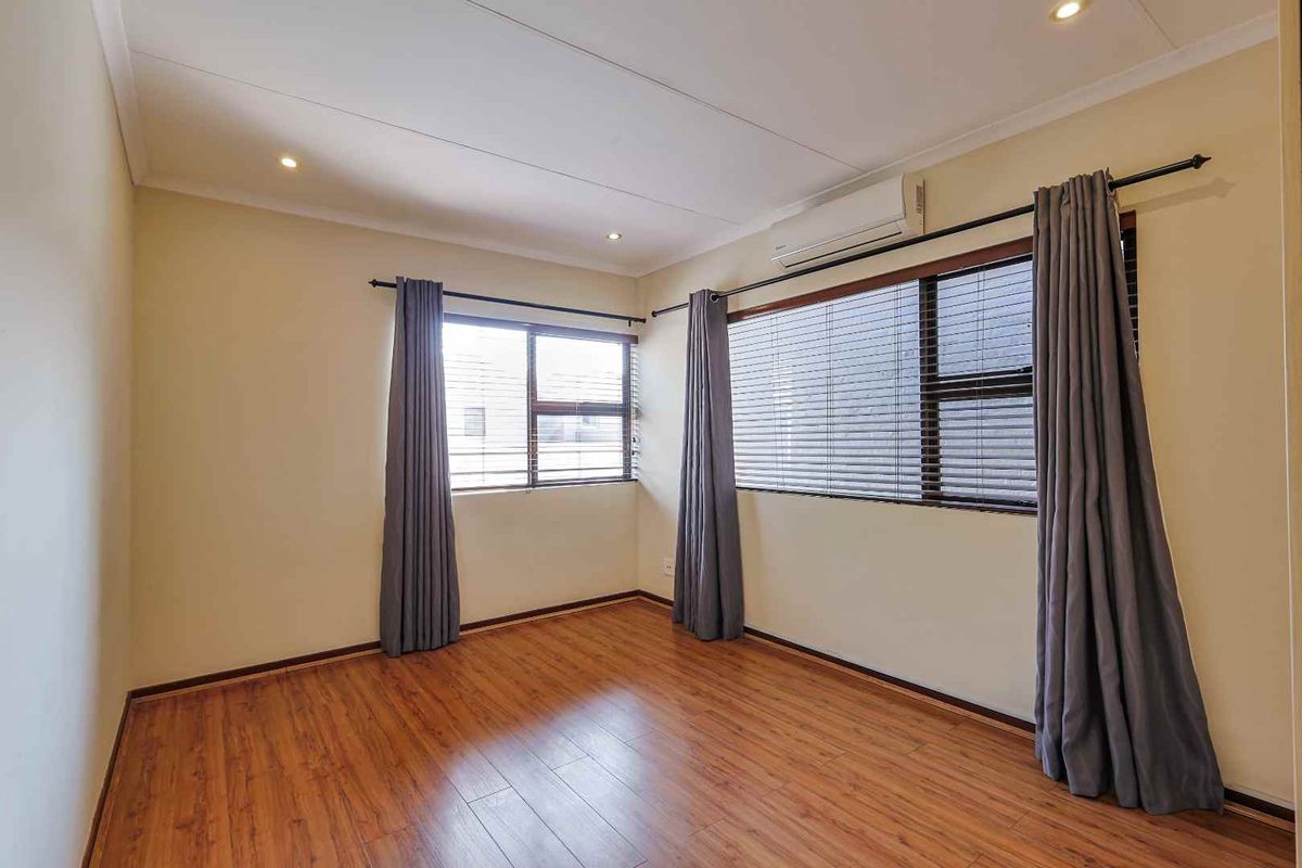 A bright and spacious bedroom featuring wood-look laminate flooring, recessed ceiling lighting, and a wall-mounted air conditioning unit.