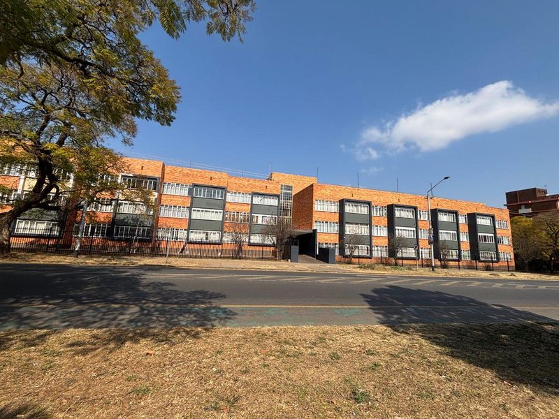 Street-facing view of a multi-story apartment building featuring a classic brick facade and secure perimeter fencing.