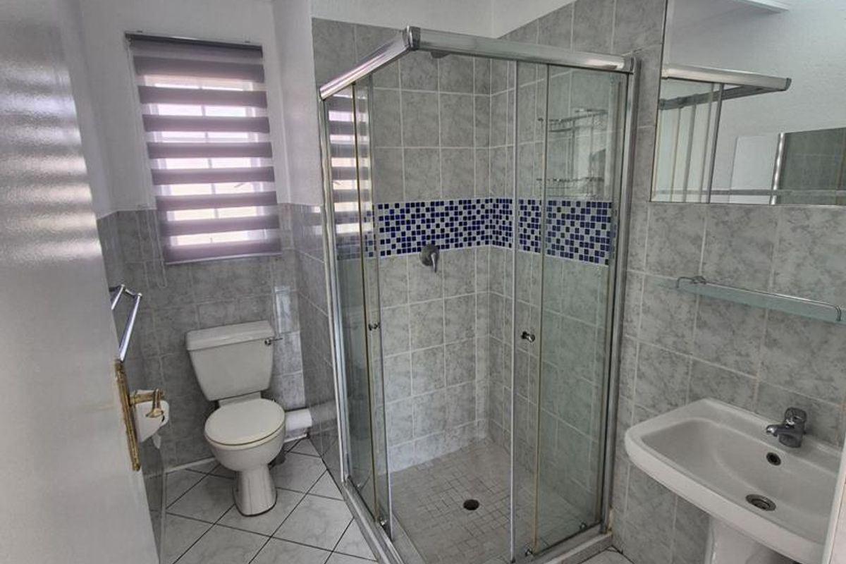 A functional bathroom featuring a corner shower enclosure, pedestal basin, and toilet, finished with neutral floor and wall tiling.