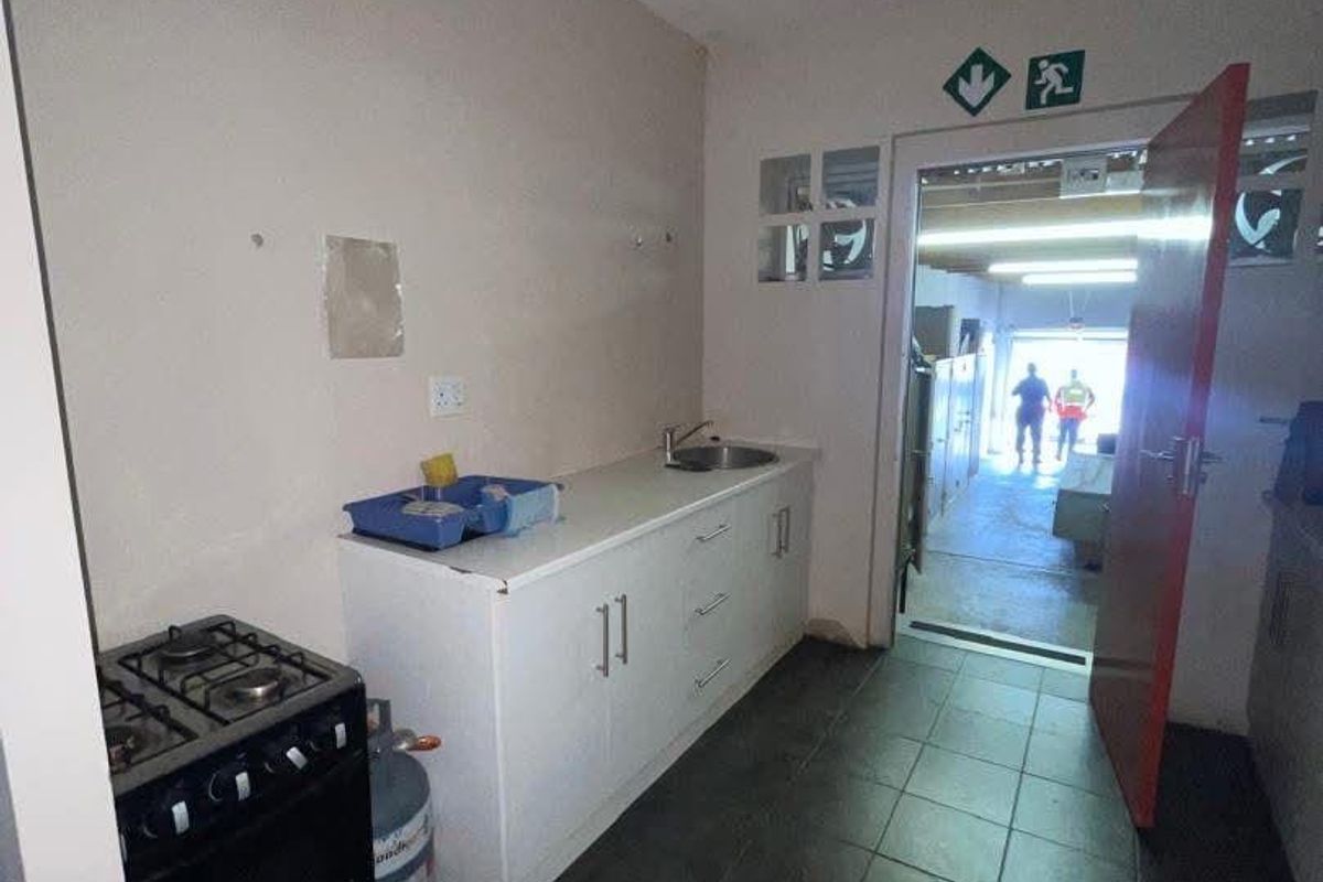 A functional kitchenette area featuring built-in cabinetry, a stainless steel sink, and a gas stove, with direct access to an adjacent workspace.