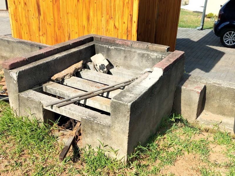 A weathered, outdoor built-in concrete braai structure located in the garden area, currently in a state of disrepair.